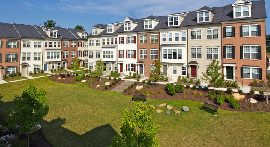 A picturesque view of multi-color townhomes set amidst a landscaped yard, accompanied by inviting benches.